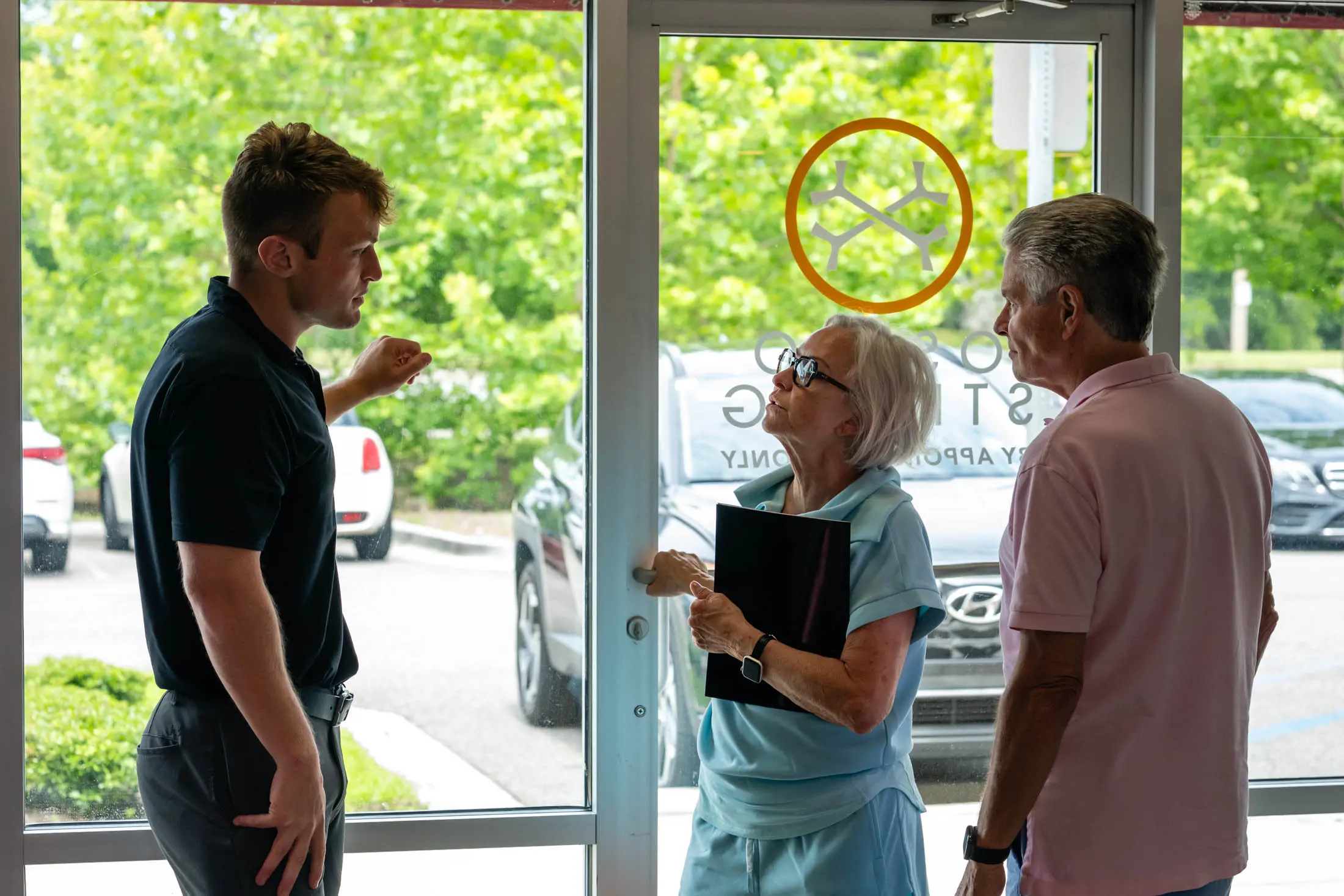 Three people talking near glass door.